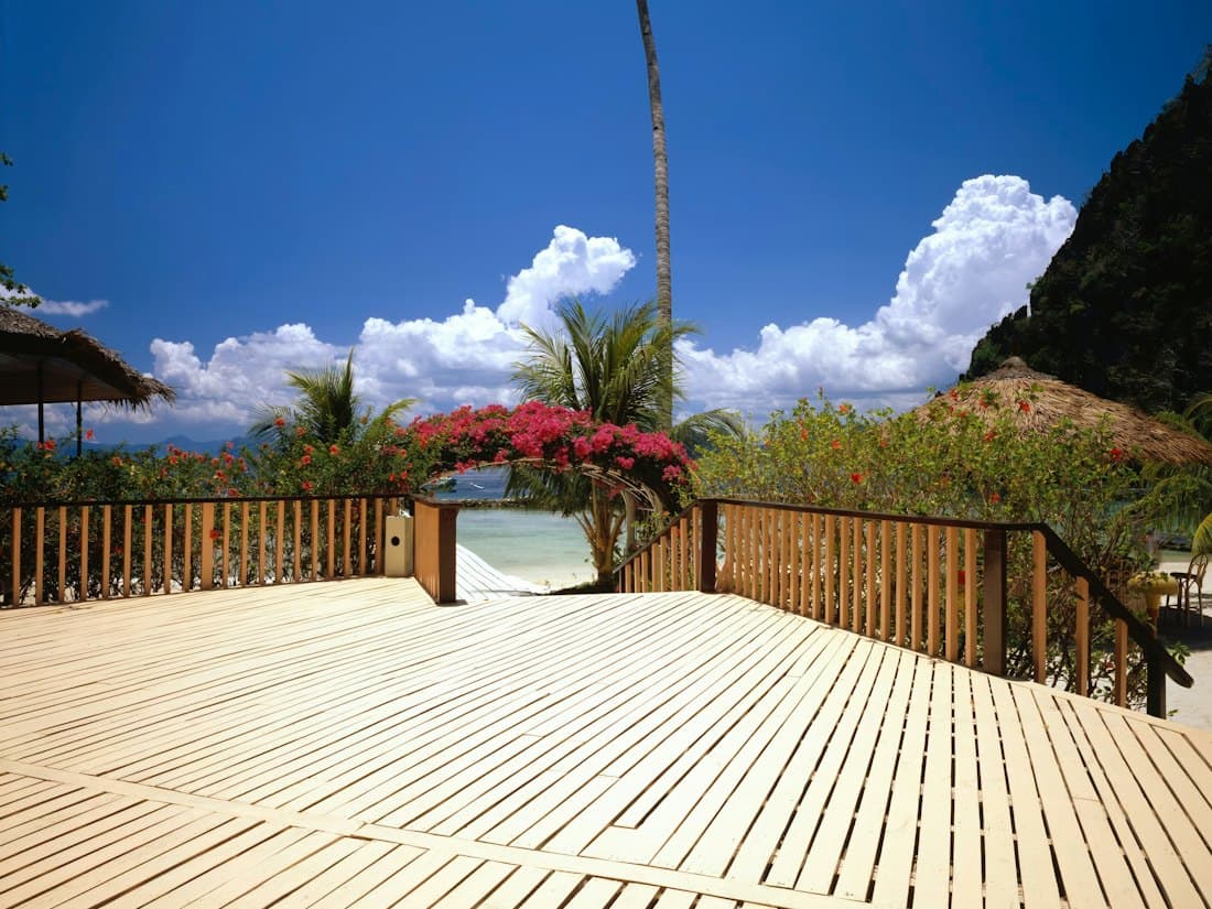 A new timber deck with railings, palm trees and a beach beyond