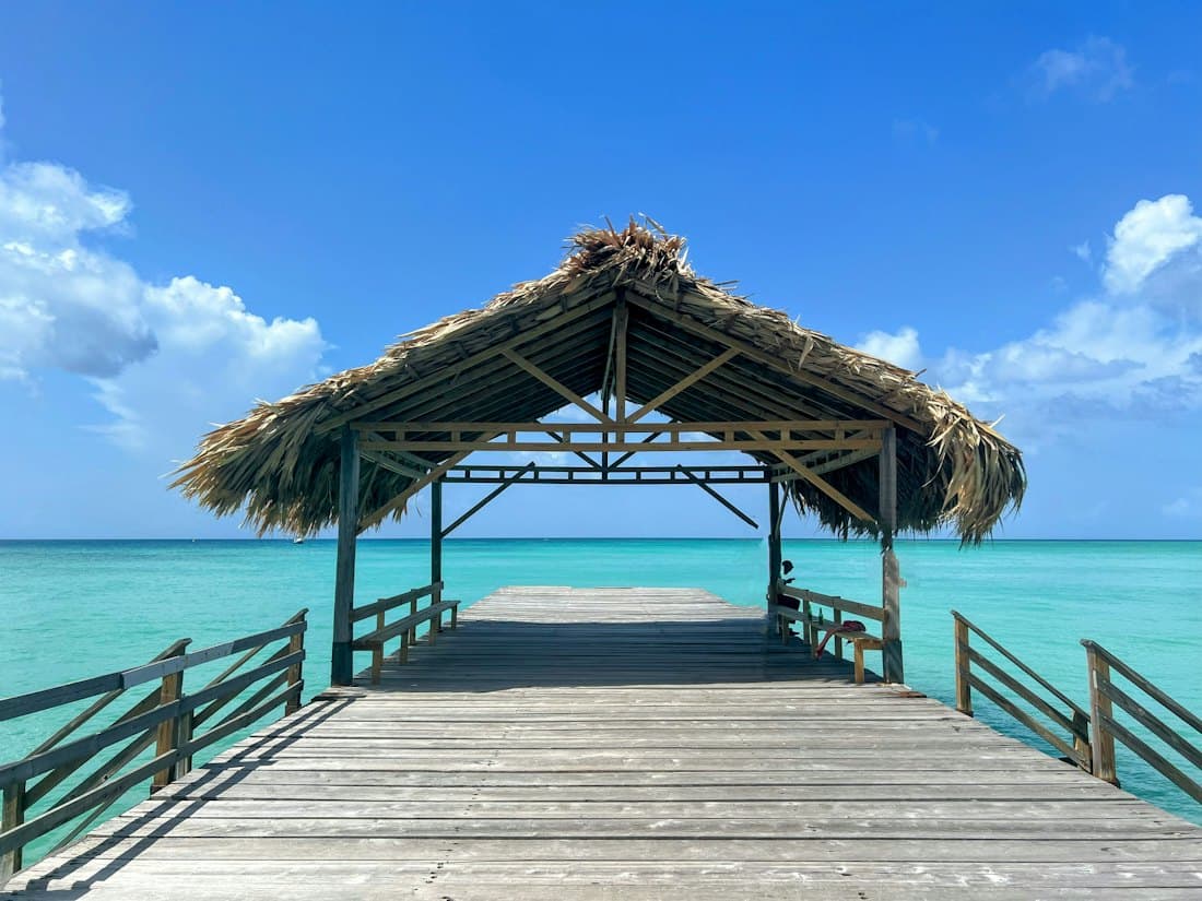 A timber dock with a thatched cabana over turquoise water