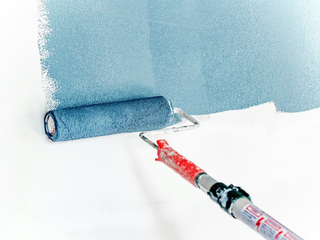 A roller laying blue paint on a white wall