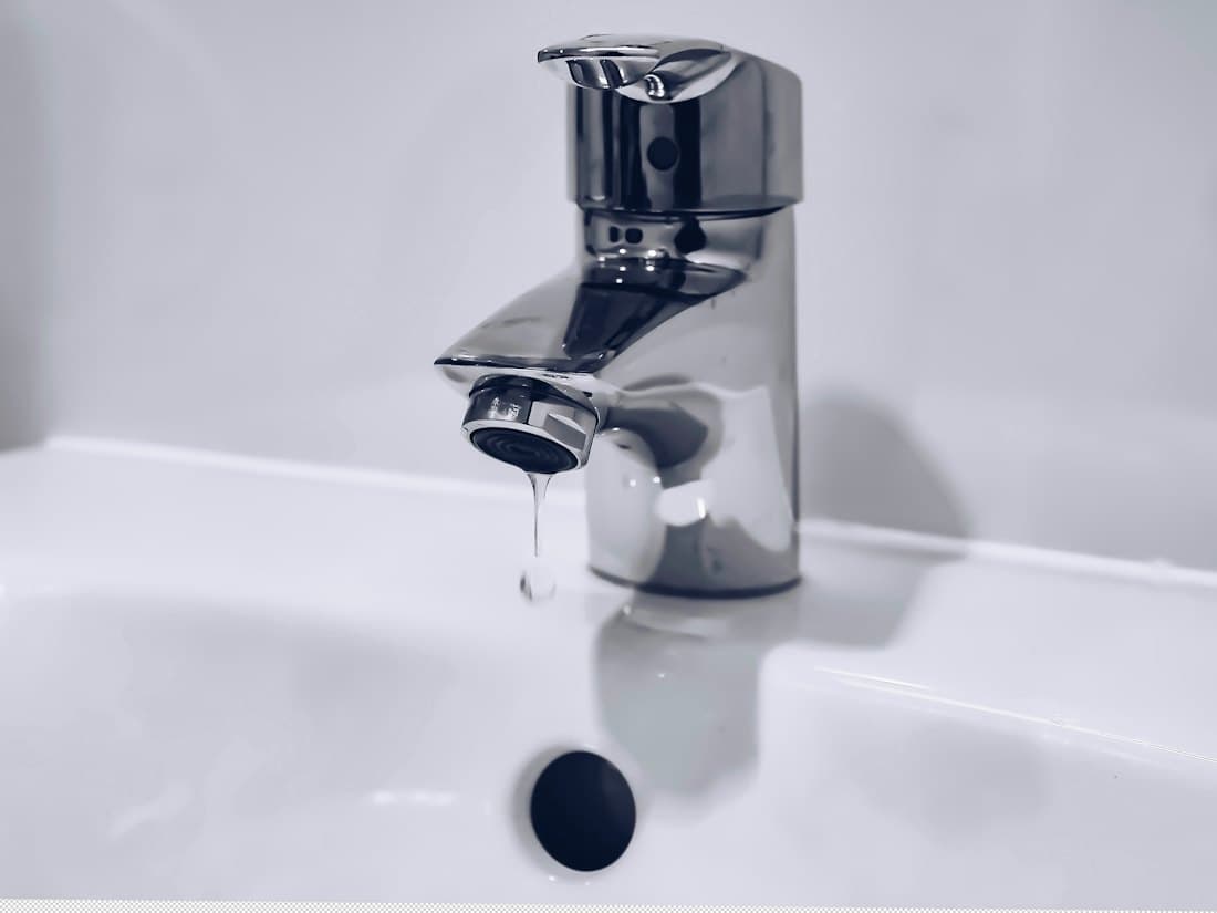 A chrome tap dripping into a white basin