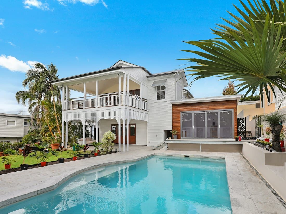A bright blue pool beside a white island home with a palm tree